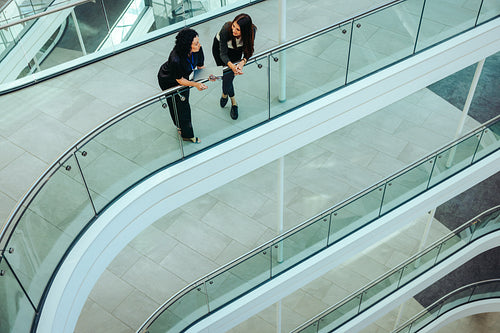 Two female coworkers conversing on a modern office flyover