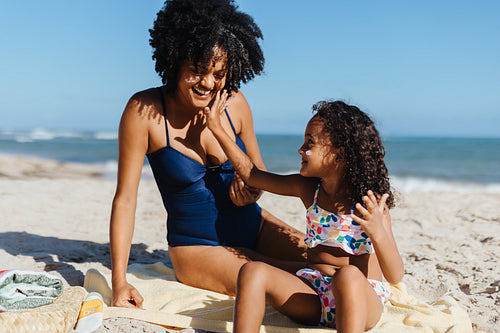 Mother and daughter applying sunscreen on a sunny beach day