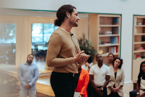 Confident male speaker presenting to a diverse audience in a warm office setting