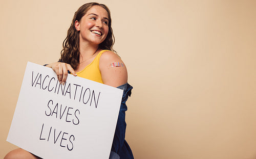 Cheerful woman with a signboard of "vaccination saves lives"