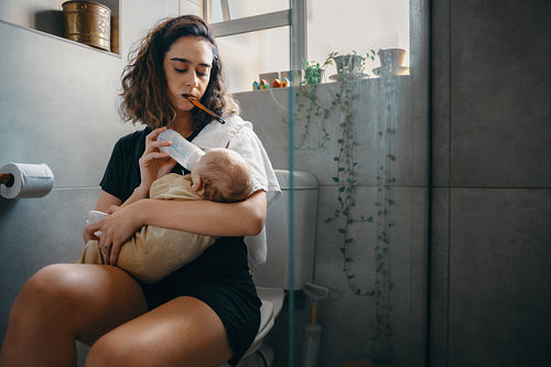 Mother feeds baby while brushing her teeth