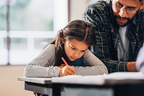 Young girl writing with a colouring pen with the help of her teacher