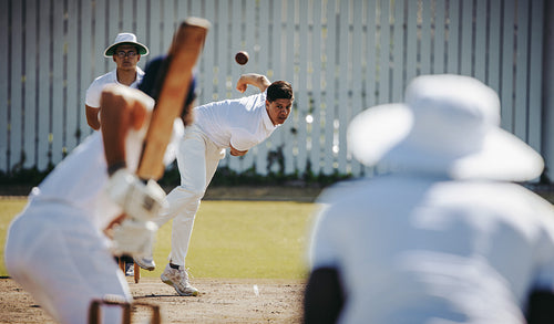 Young man bowls during an intense game of cricket in the warm sunlight