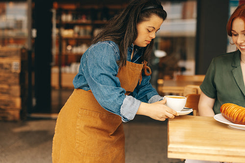 Professional waitress with Down syndrome serving a customer in a cafe