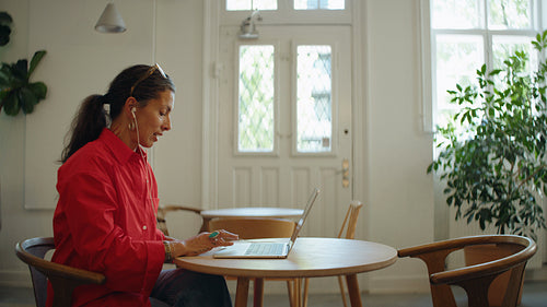 Woman talks on a laptop video call with earbuds in a cafe
