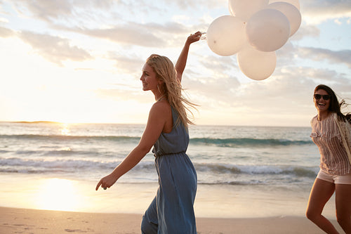 Two women running on the beach with balloons