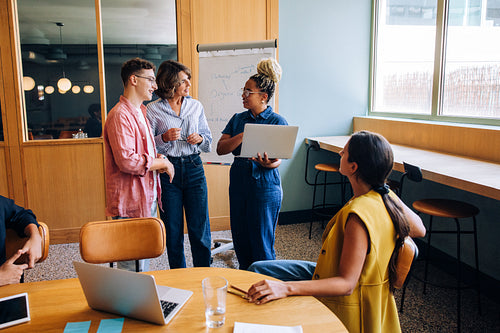 Group discussing ideas in office with laptops and presentation board