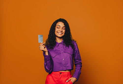Smiling woman paying with contactless credit card against vibrant orange background