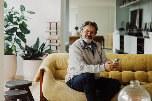 Senior man holds a smartphone while sitting at home