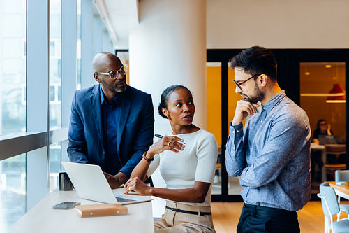 Three professionals discussing a project at a desk with a laptop