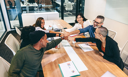 Group of cheerful businesspeople bringing their fists together in a boardroom