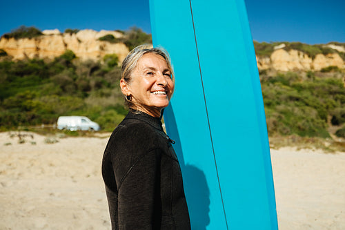 Mature woman standing by a surfboard near camper van at the beach
