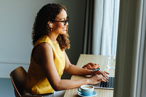 Mixed-race woman typing on laptop during a remote meeting at home office desk