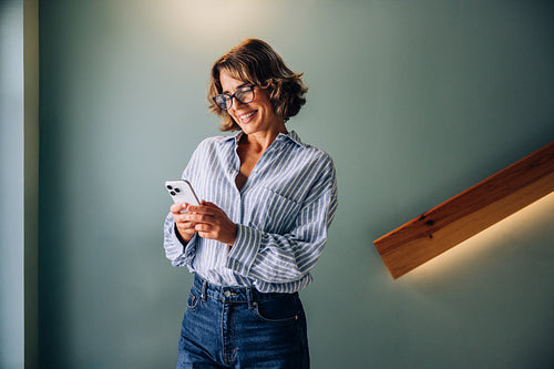 Smiling woman using her smartphone while standing in a modern setting