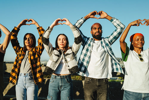 Diverse group of young adults making heart shapes with their hands outdoors