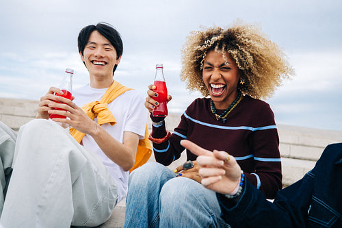 Friends laughing together while enjoying soda outdoors