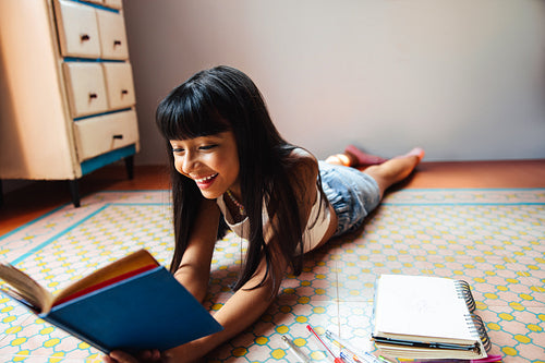 Smiling girl reading a book while lying on a patterned floor