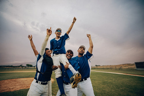 Baseball team celebrates victory with joy and camaraderie on the field as players lift a teammate