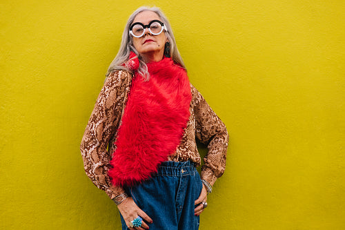Confident senior woman standing against a lemon background