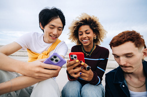 Friends smiling and sharing smartphone photos outdoors