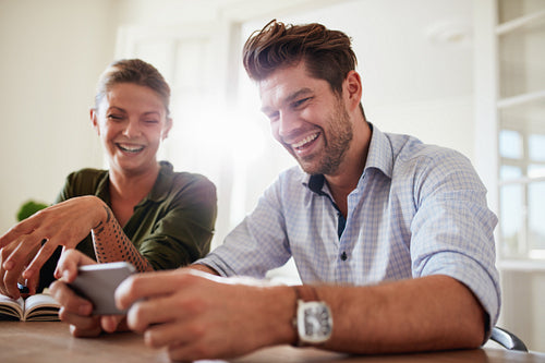 Happy young couple using cellphone at home