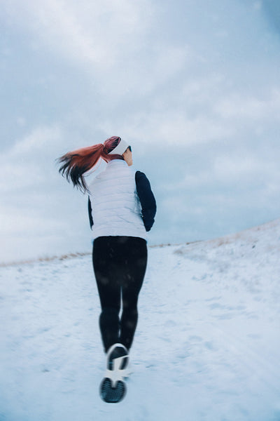 Woman running through snow during winter fitness training outdoors