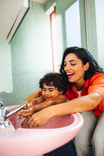 Mother and son washing hands together at a pink sink