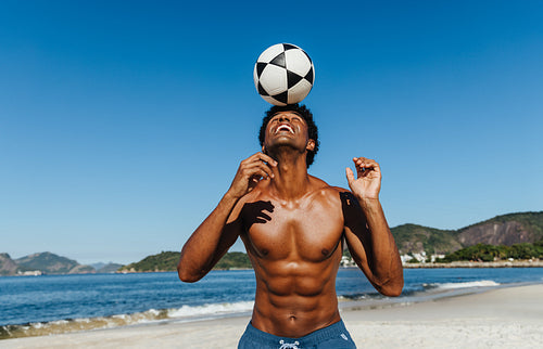 Athletic man juggling a soccer ball on a sunny beach with scenic ocean and mountain views