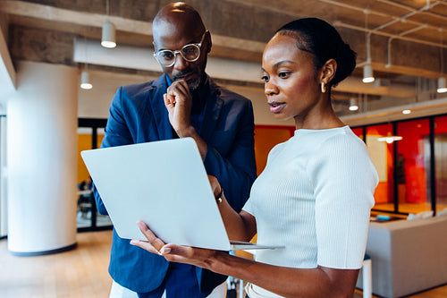 Two professionals discussing work details while looking at a laptop in an office