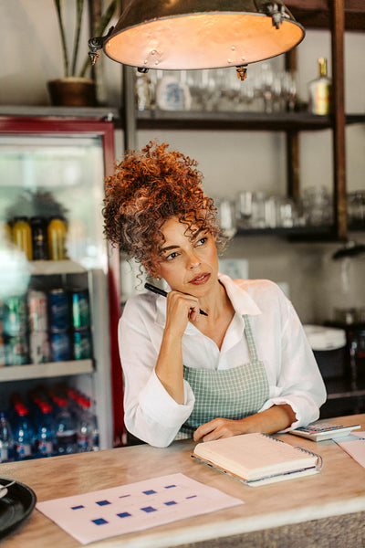 Coffee shop owner thinking while calculating her expenses