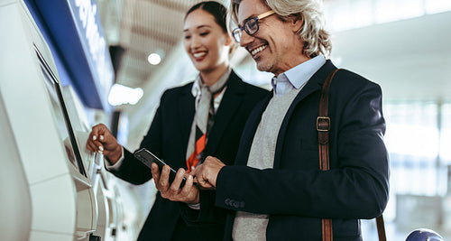 Businessman doing self check in on machine with flight attendant