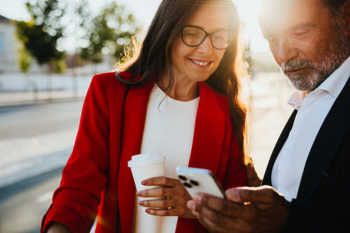 Mature professionals checking smartphone outdoors during a sunny day meeting