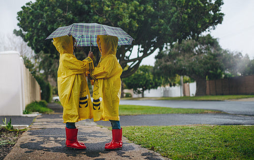 Little sisters in identical raincoats under umbrella