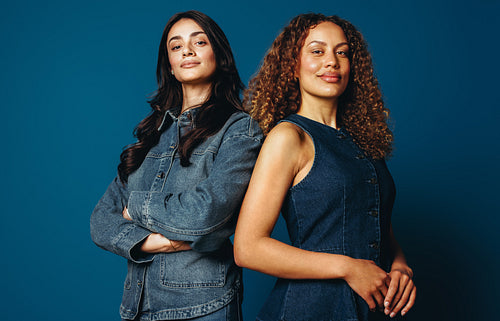 Female friends standing together in confident studio portrait against blue background