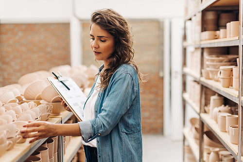 Creative businesswoman taking stock in her ceramic store