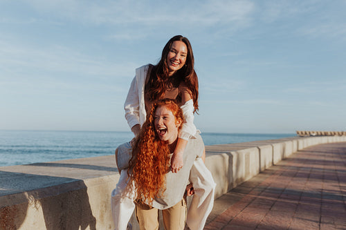 Fun-loving young woman piggybacking her friend in the promenade