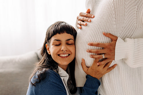 Happy young woman listening to her pregnant wife's belly
