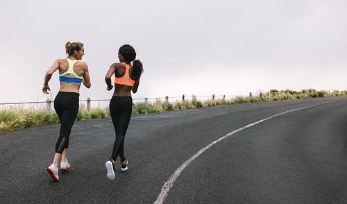 Two women athletes running on road