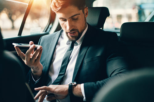 Businessman travelling by car using smart phone and checking time