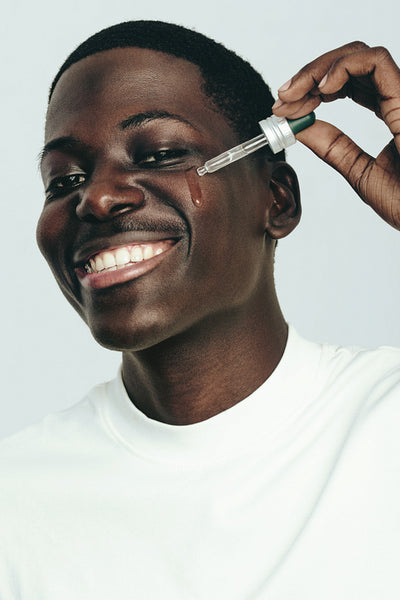 Portrait of a happy man applying face serum with a beauty dropper