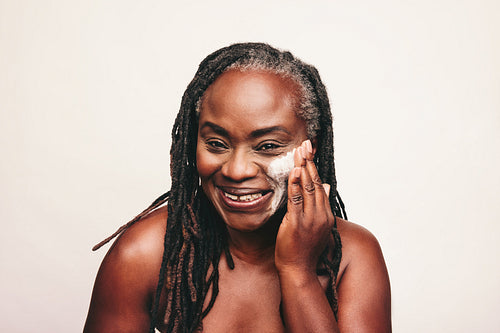 Smiling mature woman applying beauty cream on her face