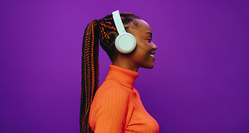 Young woman with purple two-tone braids enjoying music on headphones