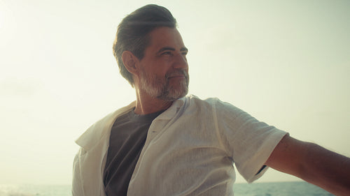 Happy mature man sailing on a calm ocean, feeling free and peaceful during sunset