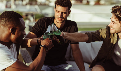 Three guys toasting their drinks outside