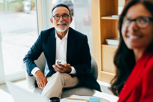 Senior businessman smiling while holding a smartphone during a business discussion