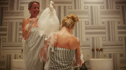 Two women enjoying a relaxing and cleansing foam ritual in a beautiful spa environment