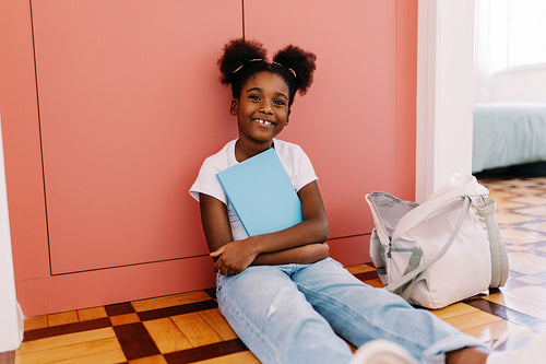 Young black girl sitting on the floor with school bag, doing homework