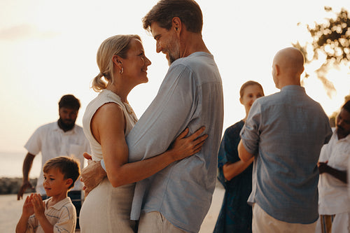 Mature couple embracing on a luxury holiday with family by the beach