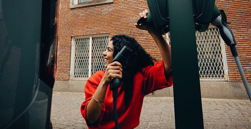Woman and her electric car are ready for charging on the street