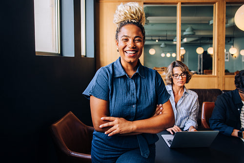Smiling woman standing confidently with colleagues working in the background